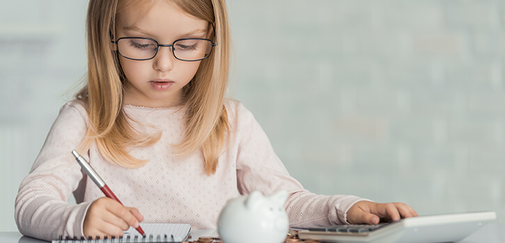Little girl wearing eyeglasses writes in notebook at table witj