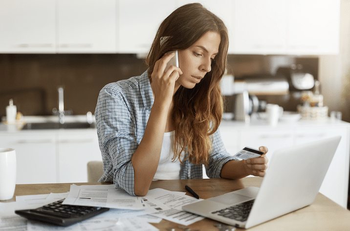 Efficient Multitasking: Woman Managing Credit Work with Laptop and Phone at Kitchen Table