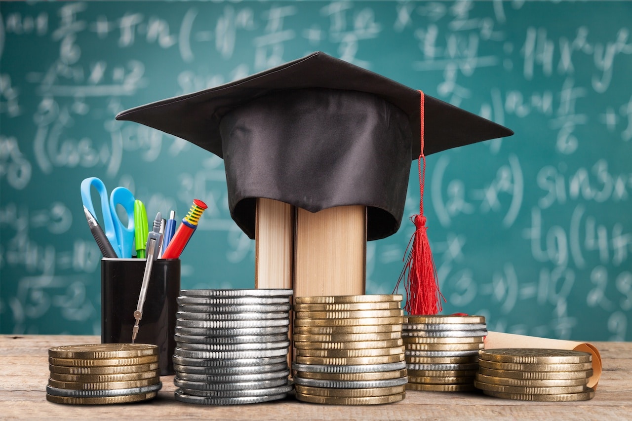 Table with Graduation Cap, Pencils, Coins, and Chalkboard - Symbolizing Achievement, Knowledge, and Financial Success