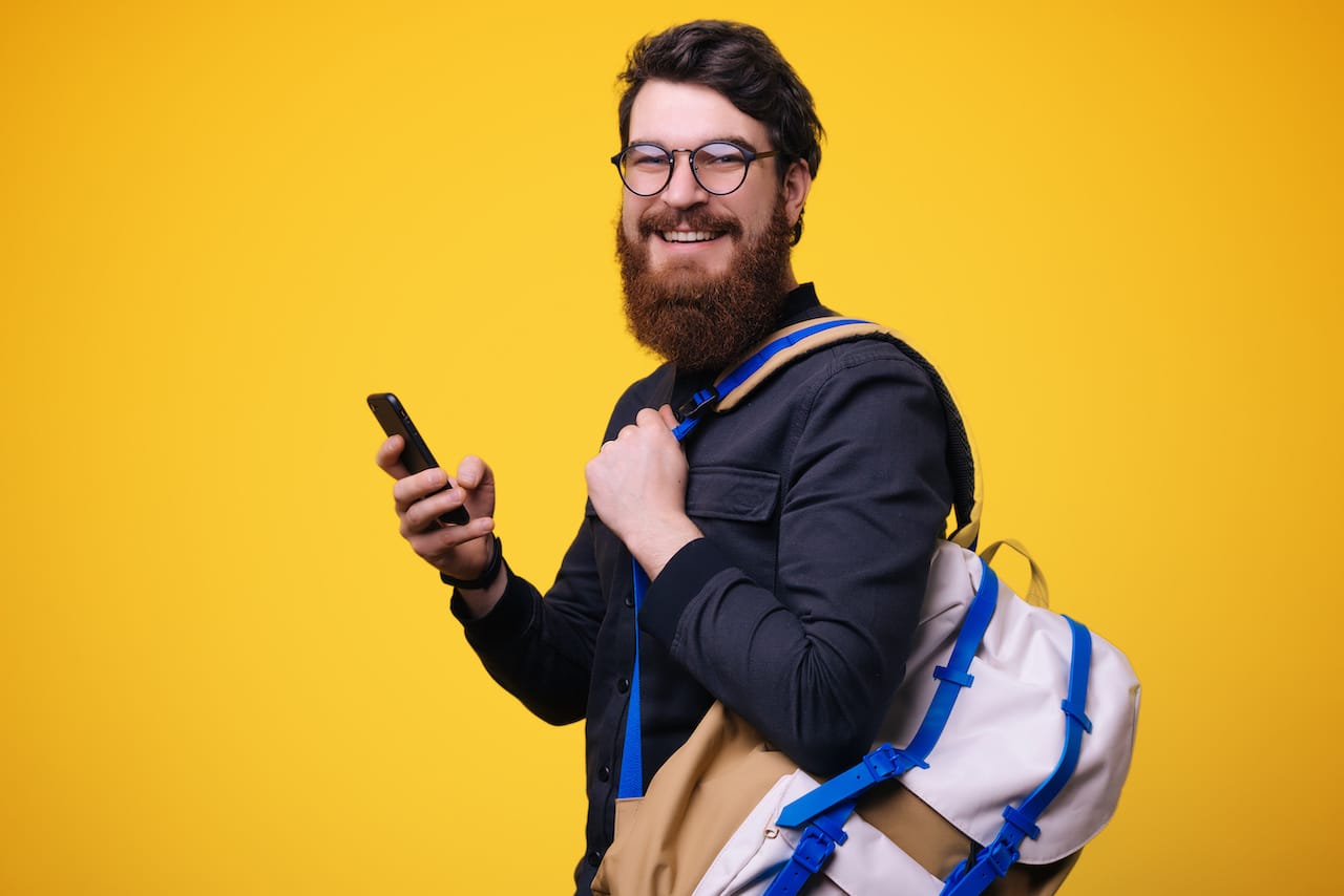 A Focused Man with Beard, Backpack, and Glasses Holds a Cellphone