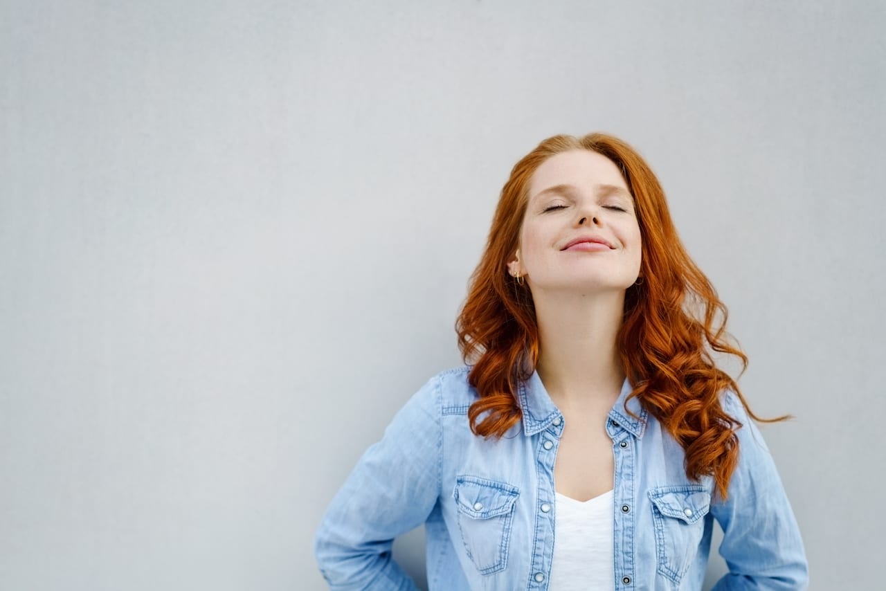 Young Woman with brown Hair and Denim Shirt Leaning Against Gray Wall